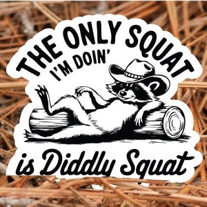 Può includere: Un adesivo in bianco e nero con un procione che indossa un cappello da cowboy e il testo "The only squat I'm doin' is Diddly Squat".