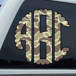 Könnte beinhalten: Ein weißer Pickup-Truck mit einem Aufkleber auf der Heckscheibe. Der Aufkleber zeigt die Buchstaben "ABC" in einem Tarnmuster aus Braun-, Beige- und Grüntönen. Der Truck steht draußen an einem sonnigen Tag.