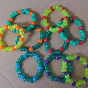 Op de afbeelding: Een set van acht kleurrijke vriendschapsarmbanden gemaakt van kleine plastic kralen. De armbanden zijn in verschillende tinten groen, oranje, rood en blauw.