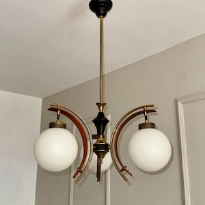 Könnte beinhalten: Ein Vintage-Kronleuchter mit drei weißen Kugelleuchten. Die Leuchte hat eine schwarz-goldene Mittelsäule mit gebogenen Holz- und Messingarmen, die die Leuchten tragen. Die Deckenhalterung ist schwarz.