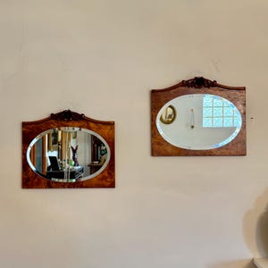 Pode incluir: Dois espelhos ovais com molduras de madeira ornamentadas, ambos com acabamento marrom escuro. Os espelhos estão pendurados em uma parede branca.