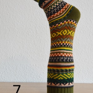 May include: A single, patterned sock with a green cuff, heel, and toe. The sock features a repeating geometric design in shades of green, yellow, orange, brown, and black. The number 7 is visible on the surface below the sock.