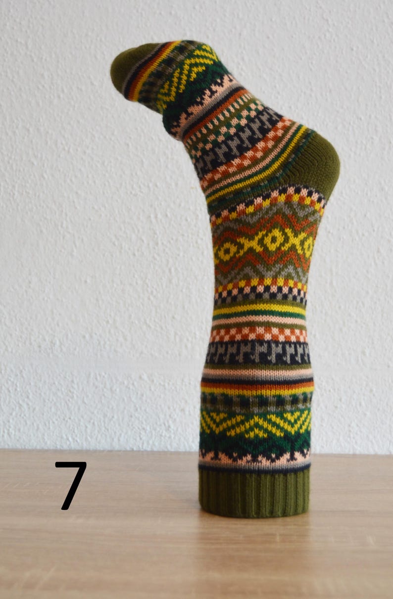 May include: A single, patterned sock with a green cuff, heel, and toe. The sock features a repeating geometric design in shades of green, yellow, orange, brown, and black. The number 7 is visible on the surface below the sock.
