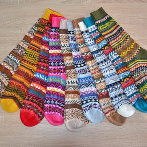 May include: A selection of patterned socks in various colours, displayed on a light wooden surface. The socks showcase diverse designs, including geometric and snowflake patterns, in shades of orange, red, pink, blue, and green.