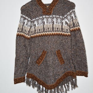 May include: A brown and white knit poncho with a hood and a front pocket. The poncho features a geometric pattern and fringe along the bottom. The design includes a pattern of llamas.