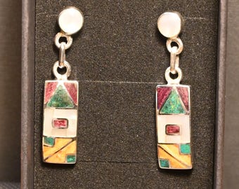 May include: A pair of silver-toned dangle earrings. Each earring features a white circular stud, connected by a chain to a rectangular pendant. The pendants have a geometric design with red, green, white, and yellow accents.