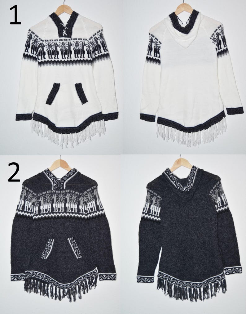 May include: Two hooded ponchos, one white and one charcoal gray, displayed on wooden hangers. Both feature a decorative pattern of figures and geometric shapes in black and white, with fringe along the bottom and pocket details.