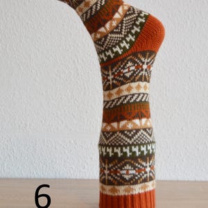 May include: A single sock with a geometric pattern in shades of orange, brown, white, and green. The sock is displayed upright, showcasing the design and texture. The number "6" is visible at the base of the sock.