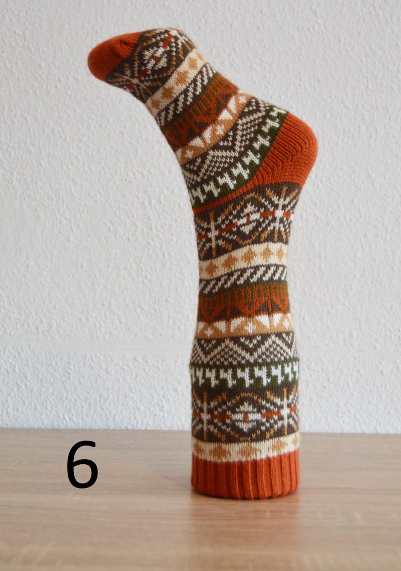 May include: A single sock with a geometric pattern in shades of orange, brown, white, and green. The sock is displayed upright, showcasing the design and texture. The number "6" is visible at the base of the sock.