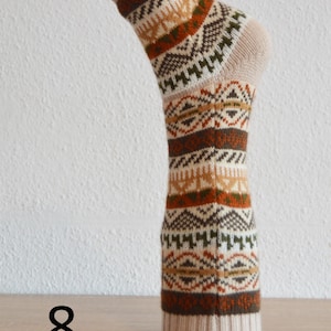 May include: A single sock with a beige and brown geometric pattern. The sock is displayed upright on a wooden surface. The number "8" is visible in black on the lower left.