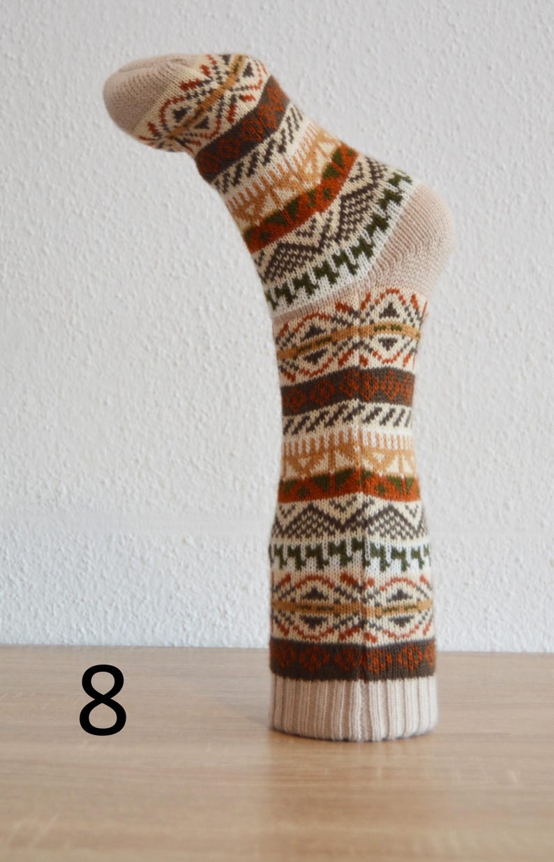 May include: A single sock with a beige and brown geometric pattern. The sock is displayed upright on a wooden surface. The number "8" is visible in black on the lower left.