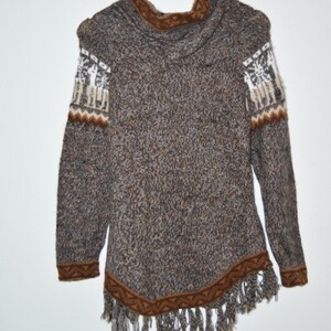 May include: A brown and gray knit sweater with a hood and fringe trim. The sweater features white and brown patterned accents on the sleeves and a brown trim along the bottom edge. The sweater is hanging on a wooden hanger.