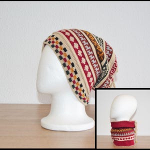 Könnte beinhalten: Eine beige, rot und schwarz gestrickte Mütze mit geometrischem Muster wird auf einem weißen Schaufensterkopf präsentiert. Die Mütze hat einen passenden Halsschmeichler in der unteren rechten Ecke. Mütze und Halsschmeichler sind aus weichem, warmem Material.