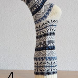 May include: A single knitted sock with a cream-coloured toe and cuff. The sock features a repeating pattern of blue, grey, and black geometric shapes. The number 4 is visible in the lower left corner.