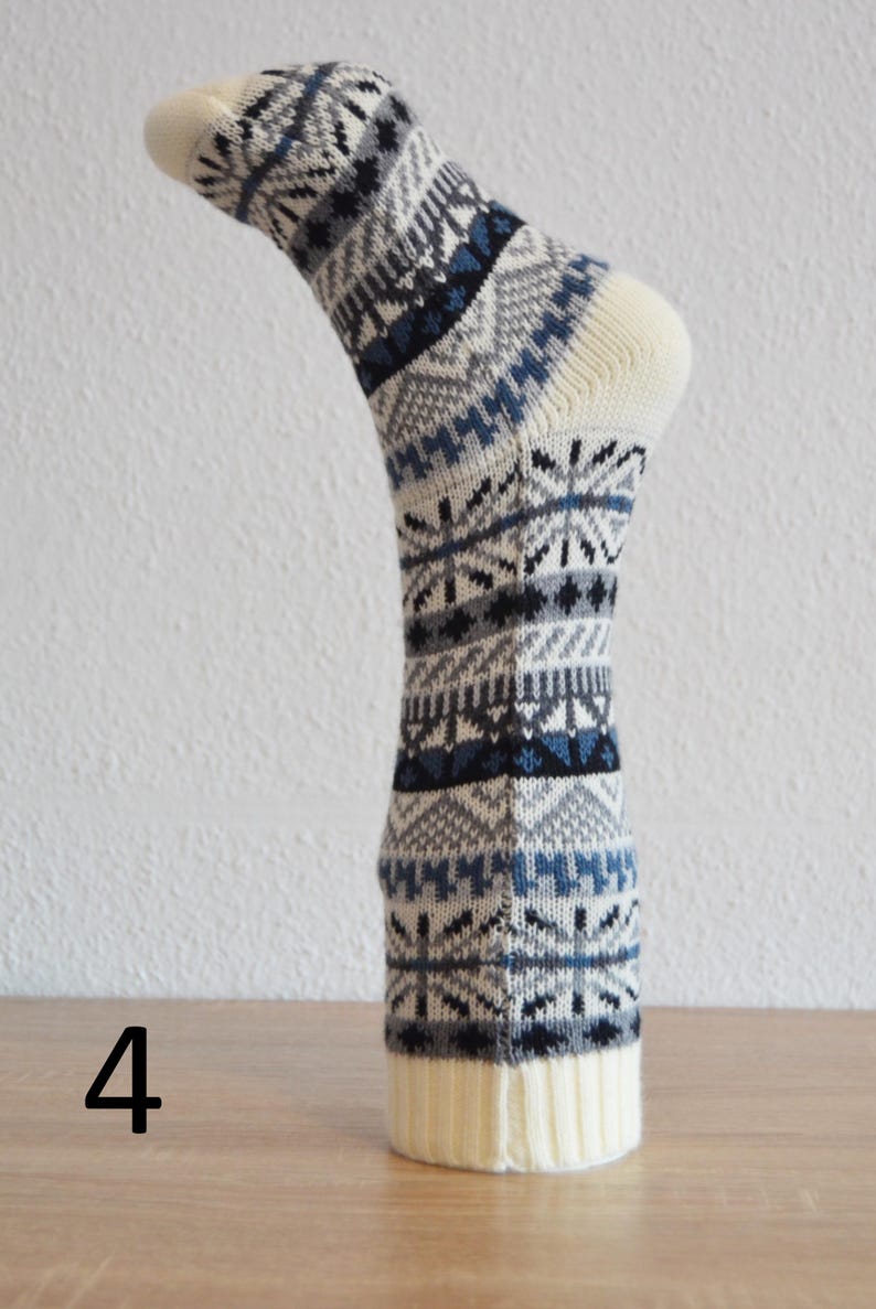 May include: A single knitted sock with a cream-coloured toe and cuff. The sock features a repeating pattern of blue, grey, and black geometric shapes. The number 4 is visible in the lower left corner.