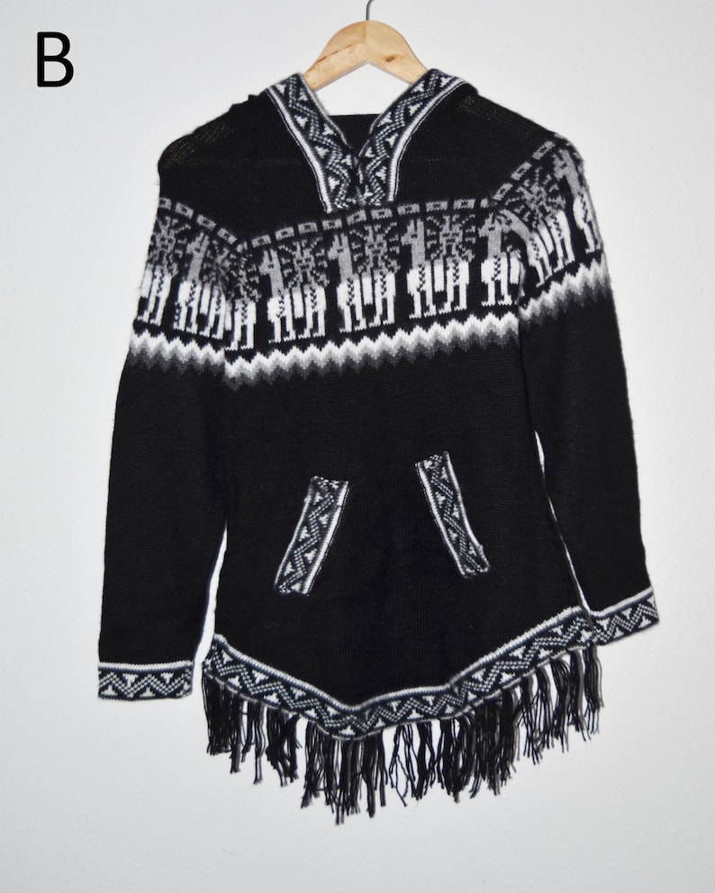 May include: Black hooded poncho with white and gray geometric patterns and fringe trim. The poncho features a front pocket and a hood with a decorative design. The design includes images of llamas.