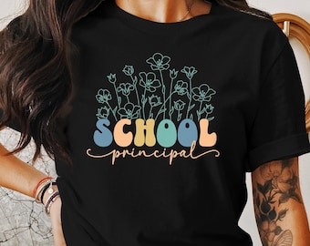 Peut inclure: T-shirt noir avec un motif de fleurs colorées et le texte "SCHOOL principal" dans une police rétro.