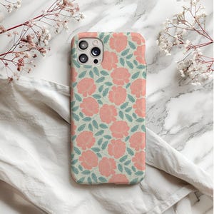 May include: A white phone case with a pink floral pattern. The case has a camera lens cutout and a raised lip around the edges.