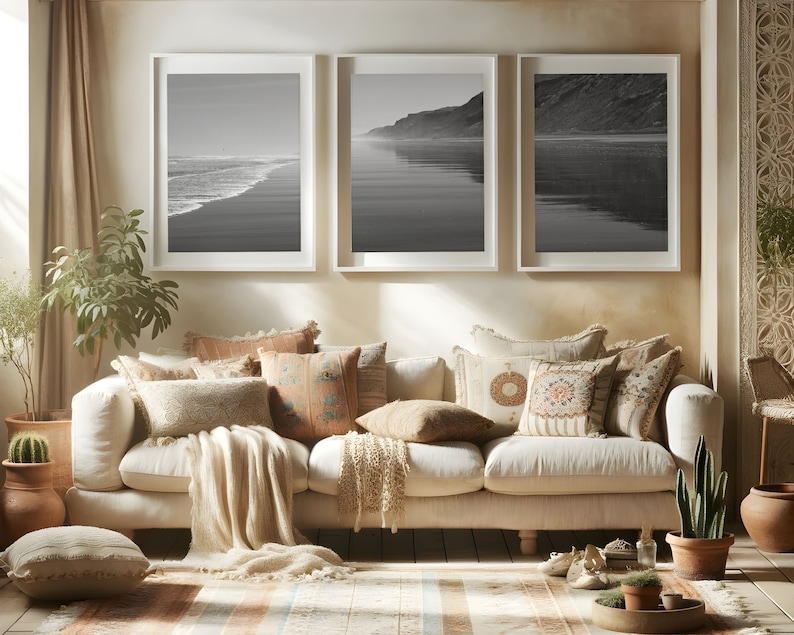 Puede incluir: Un sof&aacute; blanco con una manta de lana beige y varios cojines estampados. Tres fotograf&iacute;as en blanco y negro enmarcadas de una escena de playa cuelgan en la pared detr&aacute;s del sof&aacute;.