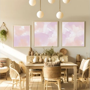 Puede incluir: Un comedor con una mesa y sillas de madera, con tres pinturas abstractas de acuarela en tonos rosa p&aacute;lido y p&uacute;rpura en la pared. La habitaci&oacute;n est&aacute; decorada con plantas, jarrones y otros elementos decorativos.