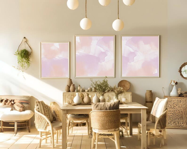 Puede incluir: Un comedor con una mesa y sillas de madera, con tres pinturas abstractas de acuarela en tonos rosa p&aacute;lido y p&uacute;rpura en la pared. La habitaci&oacute;n est&aacute; decorada con plantas, jarrones y otros elementos decorativos.