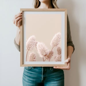 Puede incluir: Una impresi&oacute;n enmarcada de una fotograf&iacute;a que presenta un grupo de flores secas suaves de color rosa p&aacute;lido sobre un fondo beige claro.