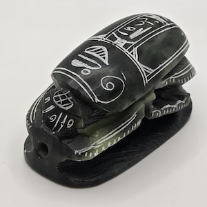 May include: A black and green carved stone scarab beetle with white markings. The scarab is a symbol of ancient Egypt and is often used in jewelry and home decor.