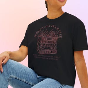 May include: Black t-shirt featuring a pink illustration of stacked books and the words "ROMANTASY BOOK CLUB". Underneath, the text reads "WHERE OUR BOOKS HAVE MAPS MORALLY GREY MEN AND MAGICAL CREATURES".