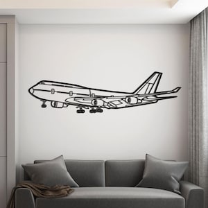 May include: A black metal wall art piece depicting a Boeing 747 airplane. The artwork is mounted on a white wall above a gray sofa. The room has a modern design with gray cabinets and a gold and white coffee table.