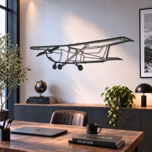 May include: A black metal wall art piece shaped like a single-engine airplane with a high-wing design, landing gear, and a propeller. The silhouette is constructed from thin metal lines, depicting the fuselage, wings, and tail section clearly.