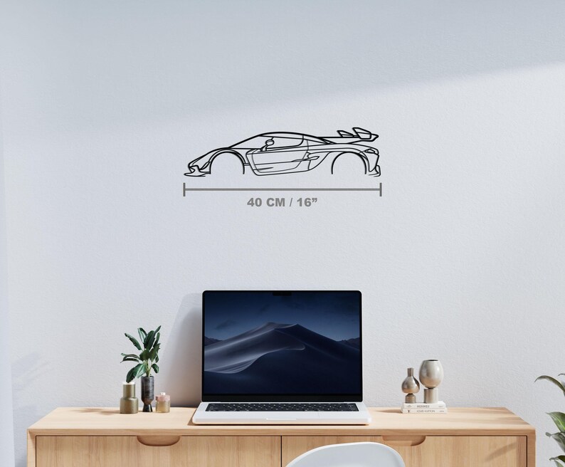 Puede incluir: Una pieza de arte mural de metal negro que representa un coche deportivo. La obra de arte es un dibujo lineal de un coche con aler&oacute;n, que mide 40 cm de largo. El coche est&aacute; montado en una pared blanca sobre un escritorio.