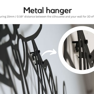 Puede incluir: Colgador de metal negro con dise&ntilde;o, montado en una pared blanca. El texto dice "Metal hanger" y "Ensuring 15mm / 0.59" distancia entre la silueta y la pared para un efecto 3D."