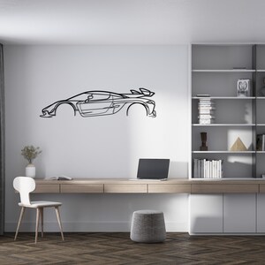Puede incluir: Arte de pared de metal negro con el contorno de un coche deportivo, montado en una pared blanca. El coche tiene un aler&oacute;n y un dise&ntilde;o aerodin&aacute;mico. La habitaci&oacute;n incluye un escritorio, una silla y una estanter&iacute;a.