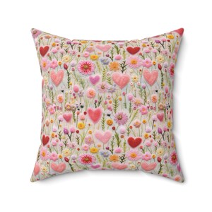 May include: A square cushion with a white background and a pattern of pink and red embroidered hearts and flowers.