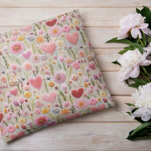 May include: A white cushion with a floral pattern featuring pink and red hearts and flowers. The cushion is on a white wooden surface.