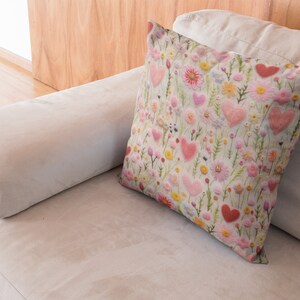 May include: A white throw pillow with a floral pattern featuring pink hearts and flowers on a light green background.