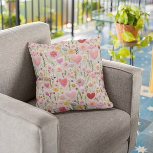 May include: A grey armchair with a pink and white floral cushion featuring embroidered hearts. The cushion has a light green background with pink, white and yellow flowers.