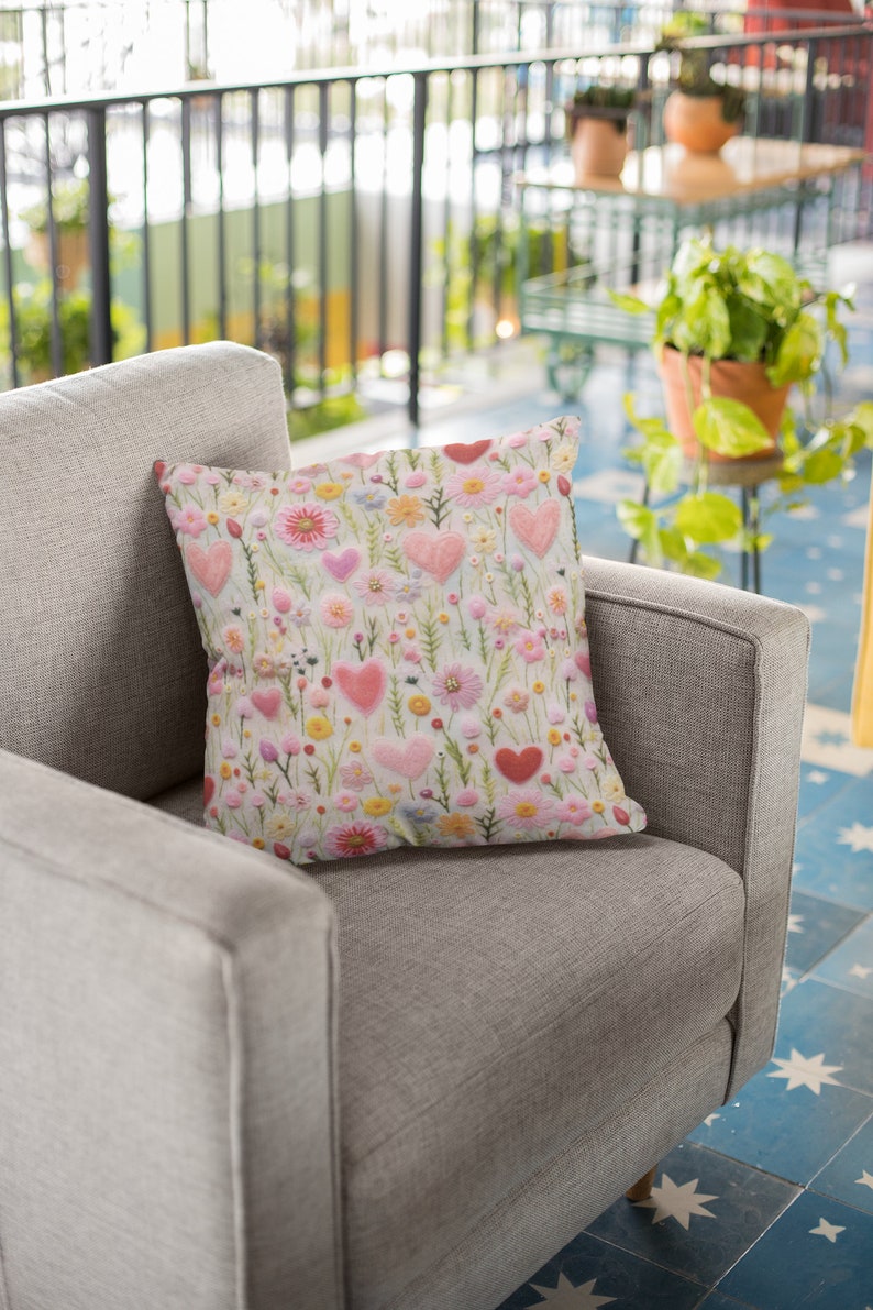 May include: A grey armchair with a pink and white floral cushion featuring embroidered hearts. The cushion has a light green background with pink, white and yellow flowers.