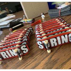 Peut inclure: Une collection de 12 planches à roulettes pour doigts rouges et blanches avec le mot "STRINGS" imprimé dessus.