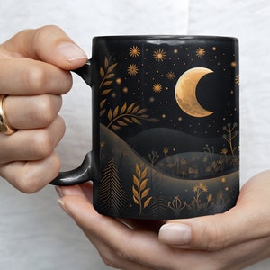 May include: Black ceramic mug with a gold crescent moon and stars design. The design features a night sky with hills and plants.