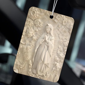 以下が含まれることがあります： 聖母マリアの宗教的な画像が描かれた白い車の芳香剤。画像は花柄で囲まれています。