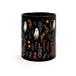 Black ceramic coffee mug featuring a whimsical Halloween design with cute white ghosts surrounded by orange, yellow, and gray autumn foliage and flowers on a dark background. The mug has a glossy finish and a large handle for comfortable use. Available in 11 oz or 15 oz sizes, this festive fall mug is both microwave safe and dishwasher safe, making it a practical yet fun seasonal drinkware choice for coffee, tea, or hot cocoa. (11 oz shown)