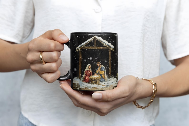 May include: Black ceramic coffee mug with a Christmas nativity scene design. The scene depicts Mary, Joseph, and baby Jesus in a stable with snow falling.