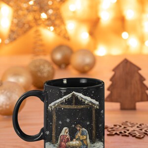 May include: Black ceramic mug with a Christmas nativity scene design. The scene depicts Mary, Joseph, and baby Jesus in a stable with a snowy roof. The background is black with white snowflakes.