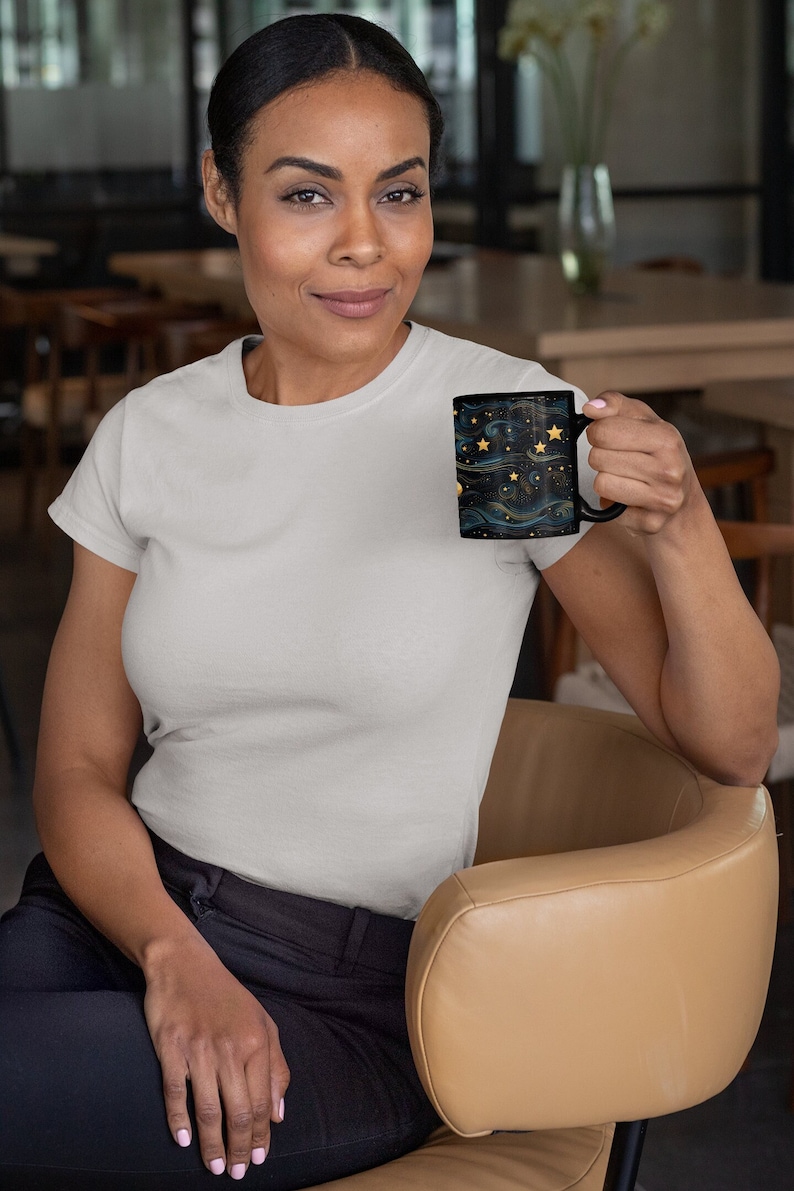 May include: A person holding a black coffee mug with a gold and blue starry night design.