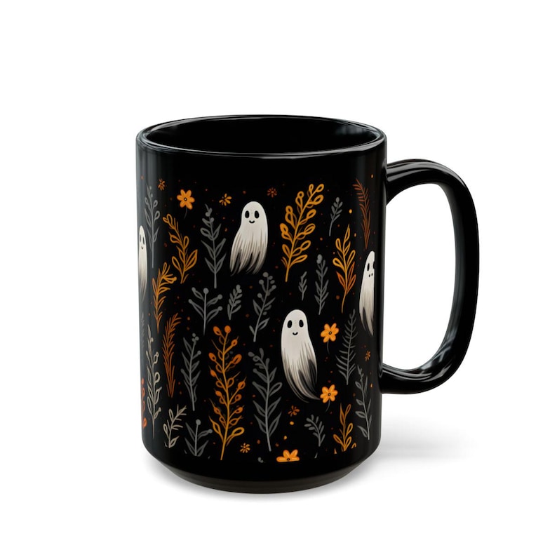 Black ceramic coffee mug featuring a whimsical Halloween design with cute white ghosts surrounded by orange, yellow, and gray autumn foliage and flowers on a dark background. The mug has a glossy finish and a large handle for comfortable use. Available in 11 oz or 15 oz sizes, this festive fall mug is both microwave safe and dishwasher safe, making it a practical yet fun seasonal drinkware choice for coffee, tea, or hot cocoa. (15 oz shown)
