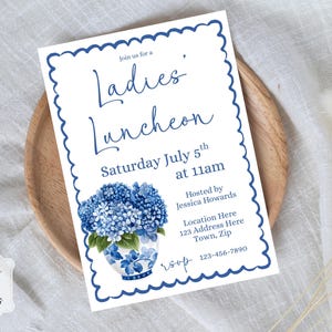 Op de afbeelding: Een rechthoekige uitnodigingskaart met een geschulpte blauwe rand en een boeket blauwe hortensia's in een vaas met motief. De tekst luidt: Join us for a Ladies' Luncheon, Saturday July 5th at 11am, Hosted by Jessica Howards, Location Here, RSVP 123-456-7890.