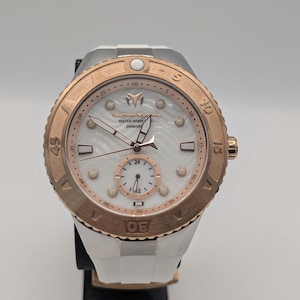 Puede incluir: Un reloj TechnoMarine blanco y oro rosa con esfera blanca y correa de silicona blanca. El reloj presenta un bisel giratorio con marcadores de minutos, una pequeña subesfera y el texto "WATER RESIST 200M/660".