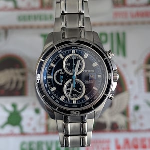 May include: A Citizen Eco-Drive Titanium watch with a dark blue face and silver-tone stainless steel band. The watch features multiple subdials, a tachymeter bezel, and the Citizen logo. The watch is a stylish accessory.