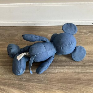 K&ouml;nnte beinhalten: Ein Denim-blaues Pl&uuml;schmaus-Spielzeug mit gro&szlig;en runden Ohren, das auf einer Holzoberfl&auml;che liegt. Das Spielzeug hat einen langen Schwanz und ein Etikett an einem Bein. Die Maus ist aus einem weichen, strukturierten Stoff gefertigt.